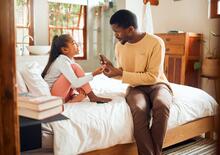 Adult checks child's glucose levels while sitting on a bed