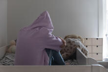 Back view of depressed teen wearing a hoodie and sitting on their bed