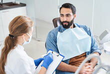 Adult in a dental chair talking to a dentist taking notes