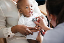 Baby on mom's lap while doctor listens to the baby's heart with a stethoscope