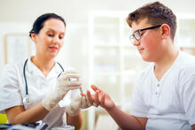 Doctor performing finger stick glucose check on teen