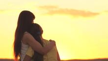 Adult hugging a child at sunset