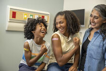 Two children in a clinic show off band-aids while an adult stands next to them