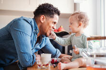Adult smiling at a Toddler sitting on the counter with food