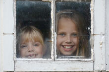 Two smiling children looking through old window with bad caulking.