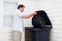 An adult putting bag of trash bag in trash container