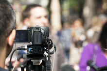 A video camera records blurred audience.