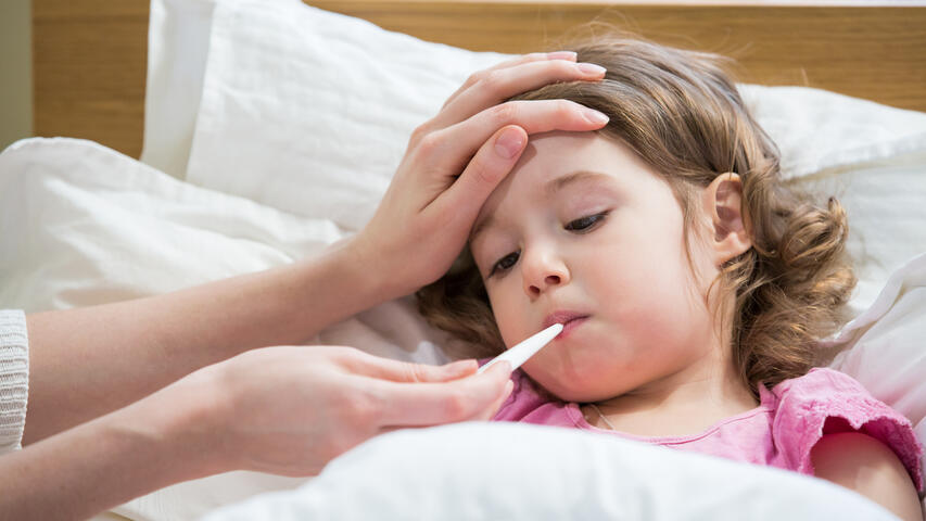 Child in bed with a fever. Parent checks temperature with hand on forehead and hold thermometer