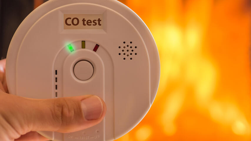 Close up of hands holding a carbon monoxide alarm with a blurred fire background