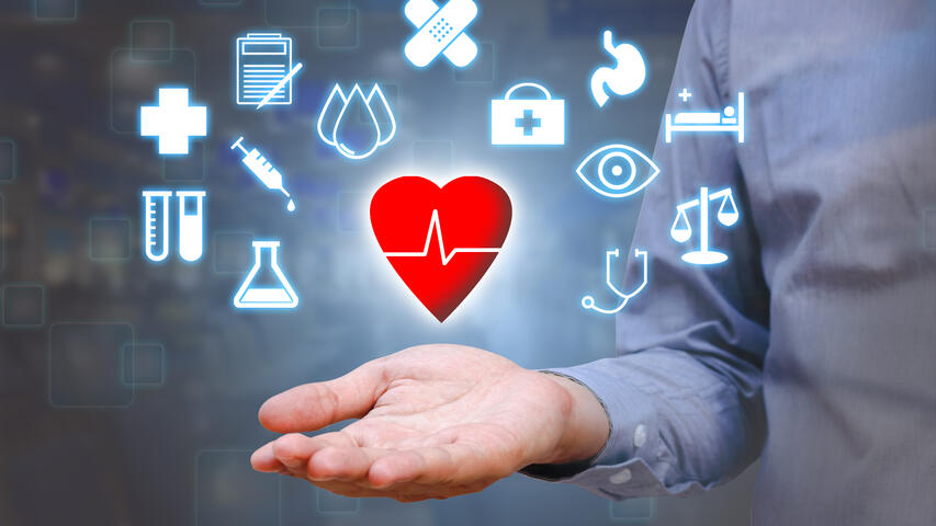 Floating red heart with EKG line across above open palm with many healthcare icons floating around.